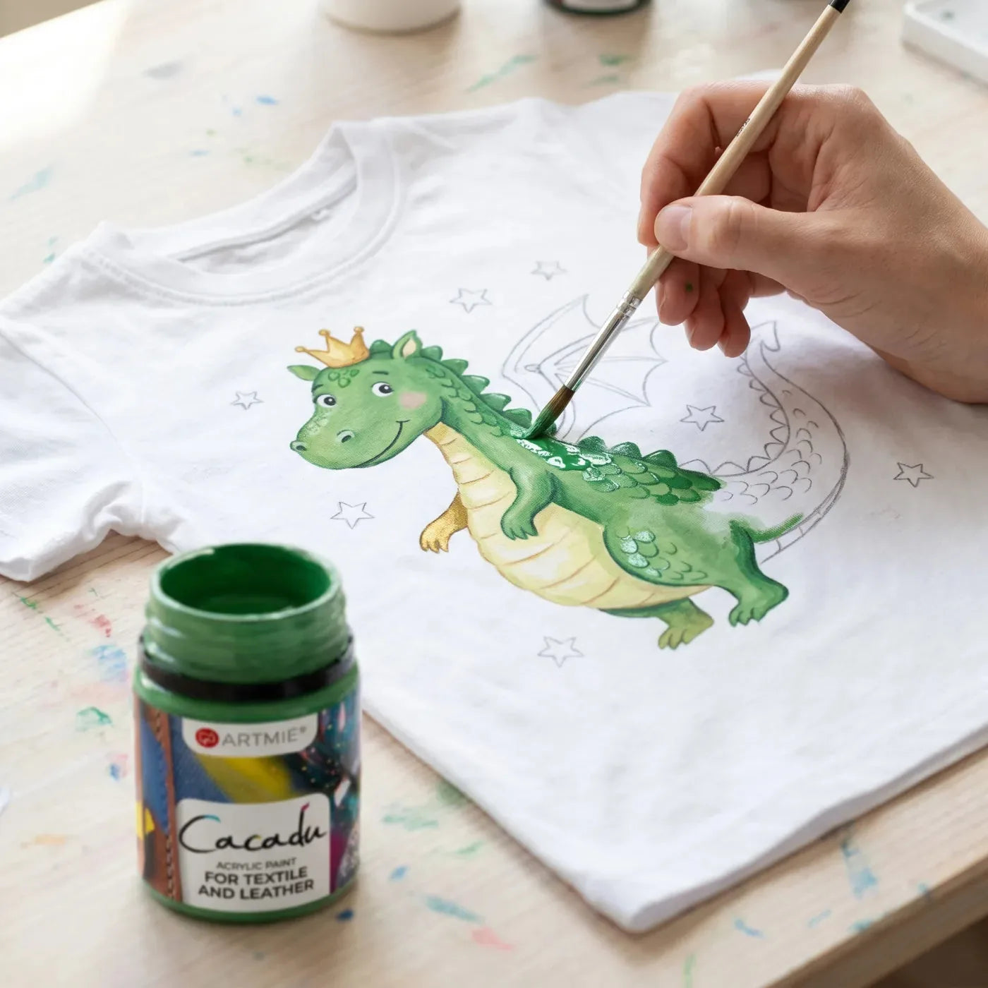 Nahaufnahme: grüner Drache wird mit Cacadu Farbe auf das Shirt gemalt